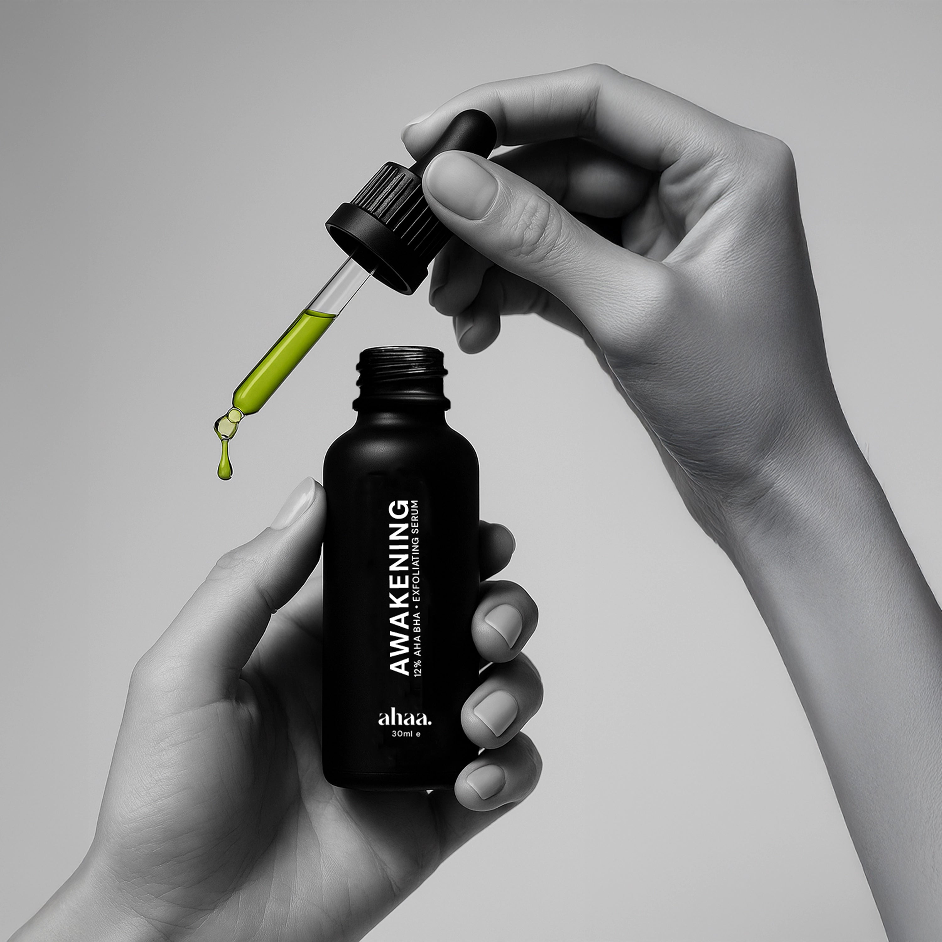 Hand holding a black dropper bottle labeled 'Awakening' with AHA and BHA green exfoliating serum liquid being dispensed.